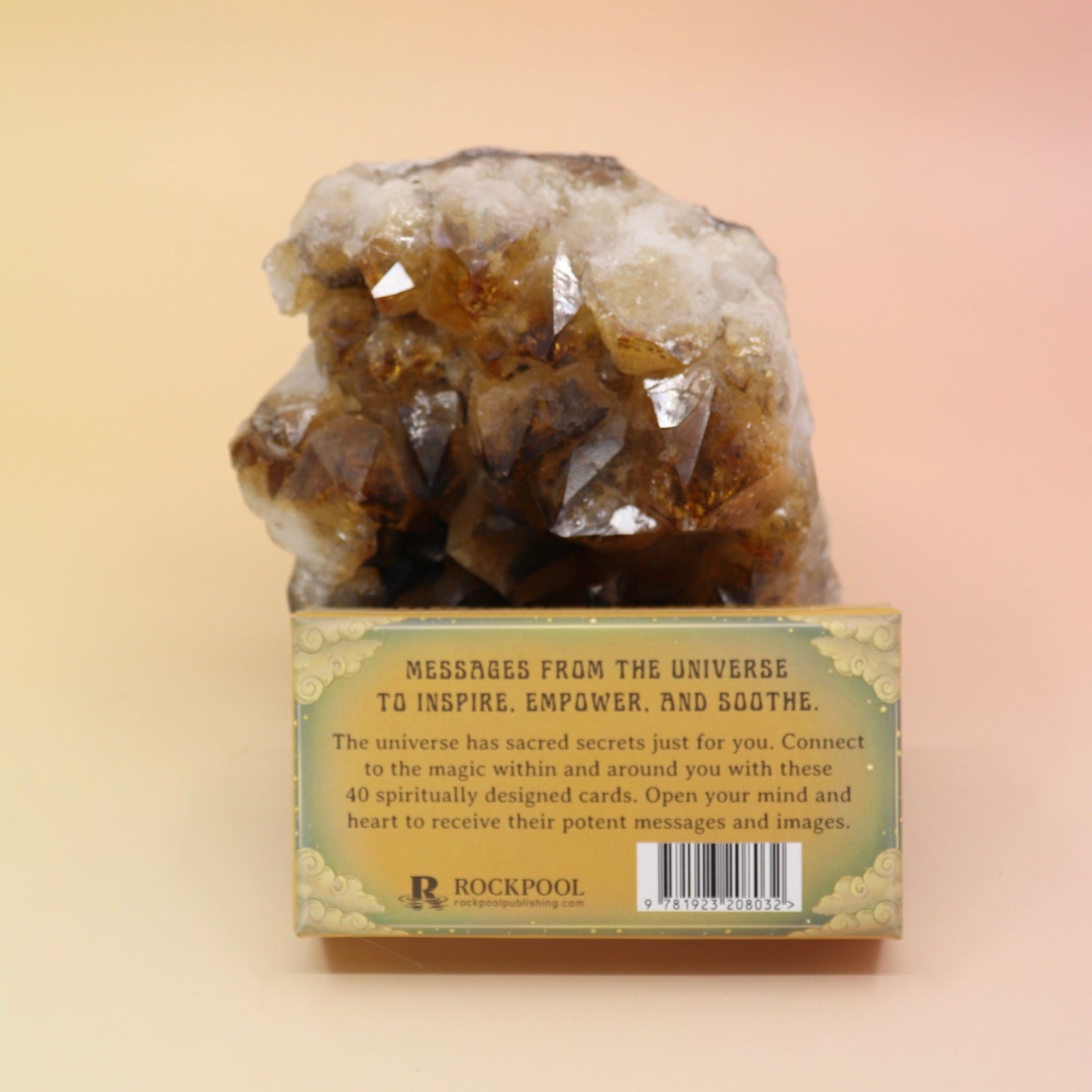 The Magical Messages from the Universe Affirmation + Divination Cards leaning against a citrine piece all on a pink and yellow background, showing off the back