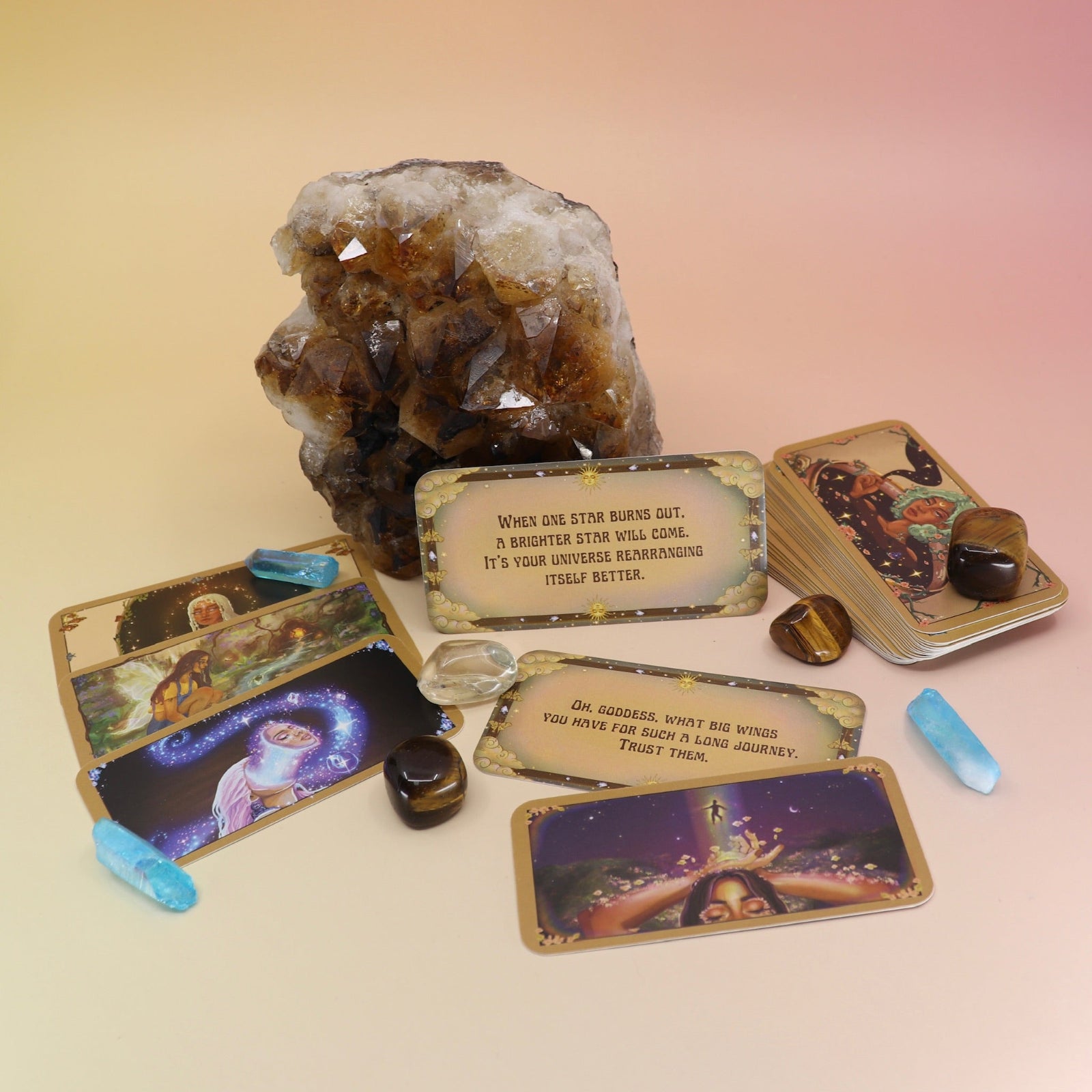 The contents of the Magical Messages from the Universe Affirmation + Divination Cards leaning against a citrine piece all on a pink and yellow background.
