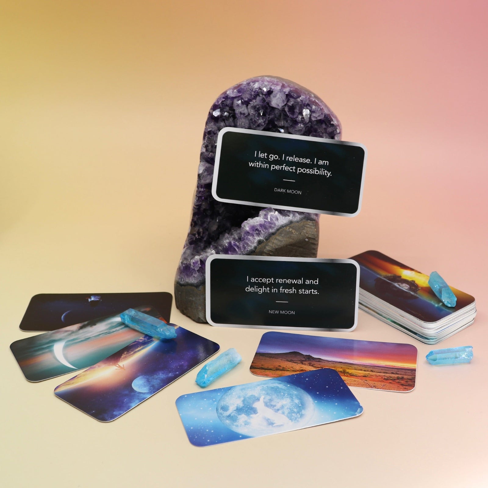 Some of the Moon Magick Affirmation + Divination Cards laying out on an amethyst piece and on a pink and yellow background.