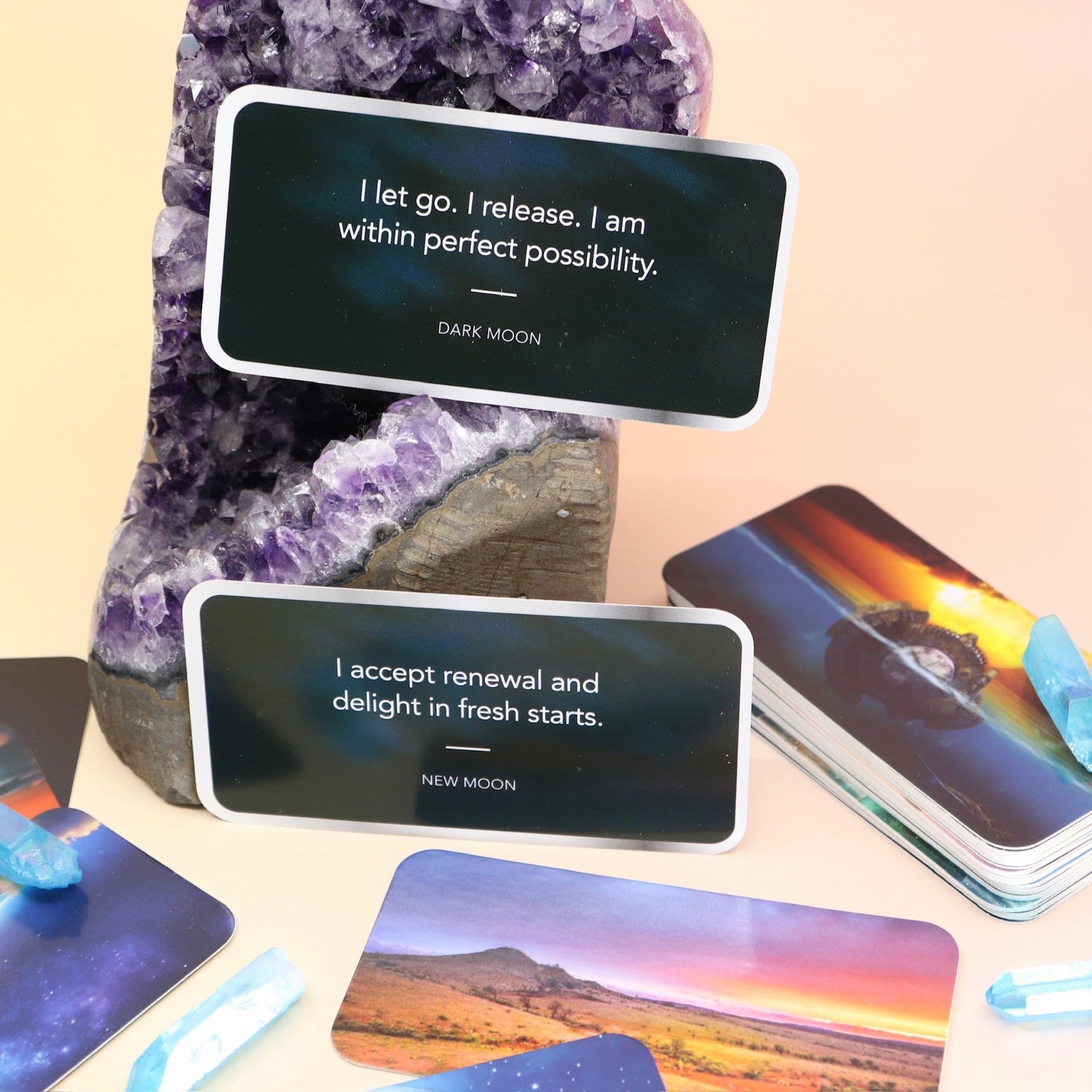Some of the Moon Magick Affirmation + Divination Cards laying out on an amethyst piece and on a pink and yellow background.