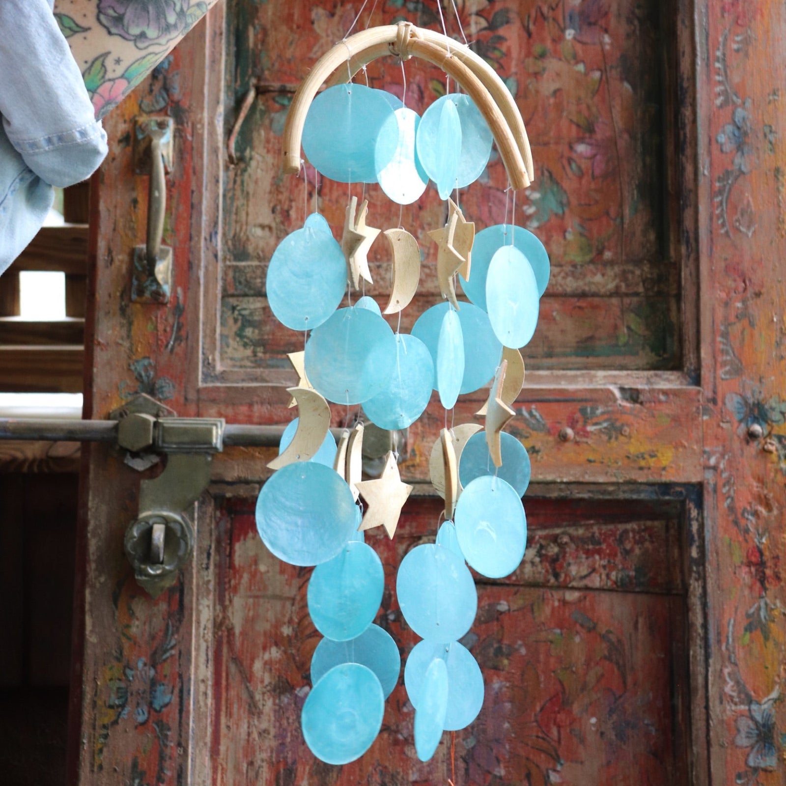 Someone holding the Moon & Stars Capiz Chime in front of a wooden door.