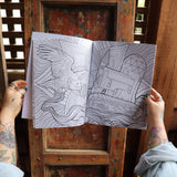 Someone holding the Psychedelic Cats Coloring Book open in front of a wooden background, showing off the pages.