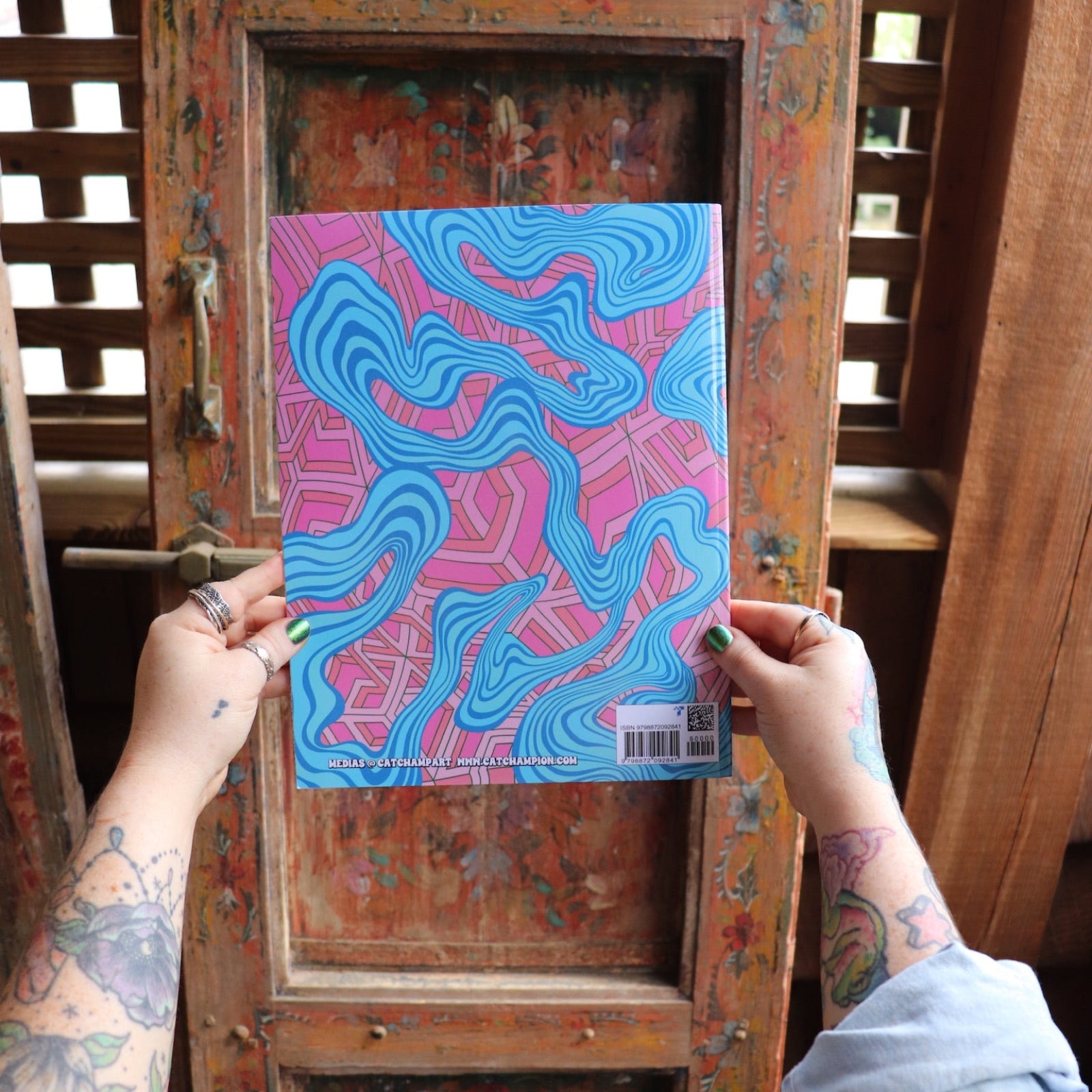 Someone holding the Psychedelic Cats Coloring Book in front of a wooden background, showing off the back.