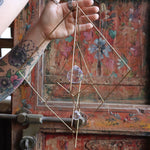 The Prisma Hanging #27 Brass Suncatcher in front of a wooden background.