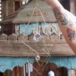 The Prisma Hanging #27 Brass Suncatcher in front of a wooden background.