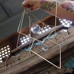 The Prisma Hanging #27 Brass Suncatcher in front of a wooden background.