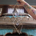 The Prisma Hanging #27 Brass Suncatcher in front of a wooden background.