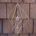 The Prisma Hanging #27 Brass Suncatcher in front of a wooden background.