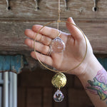 Someone holding the Prisma Hanging #22 Brass Round Suncatcher in front of a wooden background.