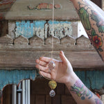 Someone holding the Prisma Hanging #22 Brass Round Suncatcher in front of a wooden background.