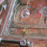 An up-close image of someone holding the Prisma Hanging #22 Brass Round Suncatcher in front of a wooden background.