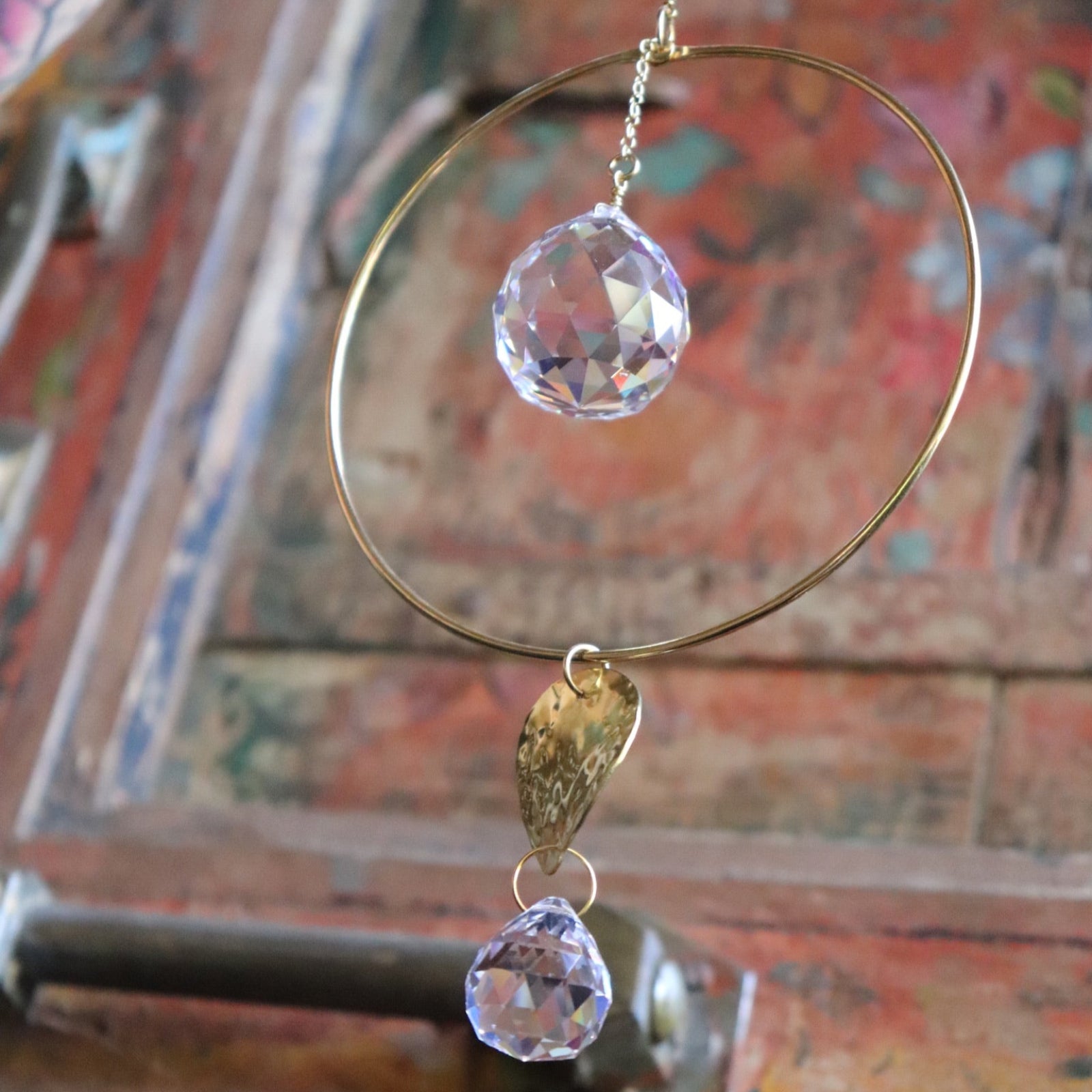 An up-close image of someone holding the Prisma Hanging #22 Brass Round Suncatcher in front of a wooden background.