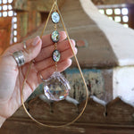 Someone holding the Prisma Hanging #33 Abalone Shell Brass Suncatcher in front of a wooden background.