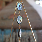 An up-close image of the abalone discs on the Prisma Hanging #33 Abalone Shell Brass Suncatcher in front of a wooden background.