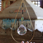 Someone holding the Prisma Hanging #33 Abalone Shell Brass Suncatcher in front of a wooden background.