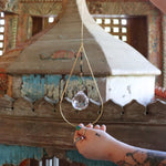 Someone holding the Prisma Hanging #33 Abalone Shell Brass Suncatcher in front of a wooden background.