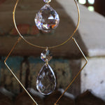 An up-close image of someone holding the Prisma Hanging #42 Brass Geometrical Suncatcher in front of a wooden background.