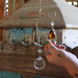 Someone holding the Prisma Hanging #35 Brass Suncatcher in front of a wooden background.