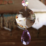 An up-close image of someone holding the Prisma Hanging #36 Brass & Purple Suncatcher in front of a wooden background, showing off the crystals.
