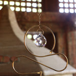An up-close image of someone holding the Prisma Hanging #36 Brass & Purple Suncatcher in front of a wooden background.