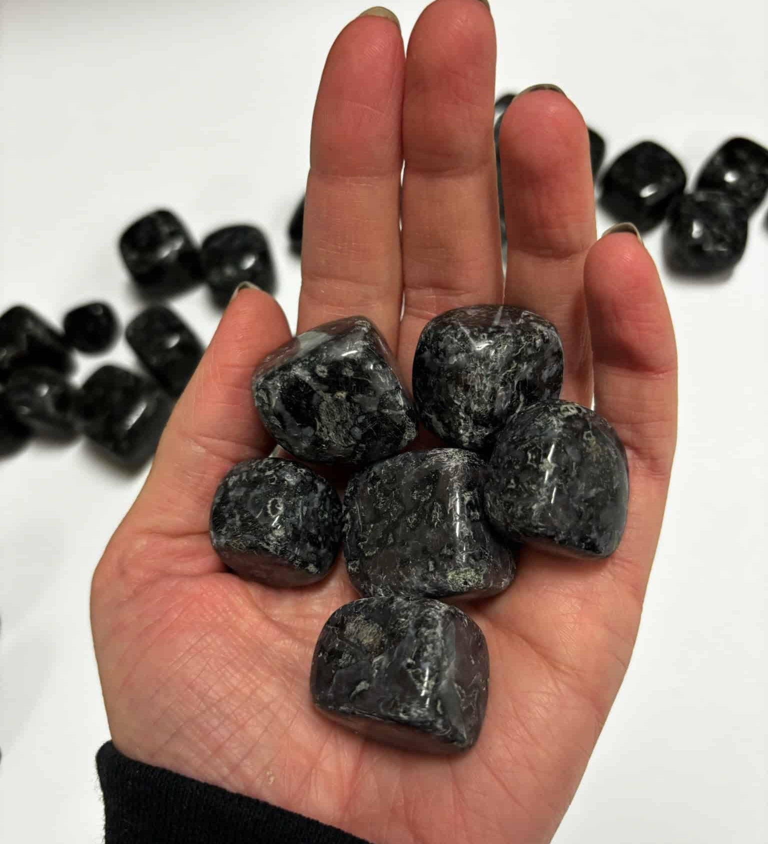 Hand holding several polished Indigo Gabbro tumbled stones in shades of deep gray and black