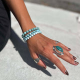 Hand wearing multiple Larimar bracelets and rings on a light background