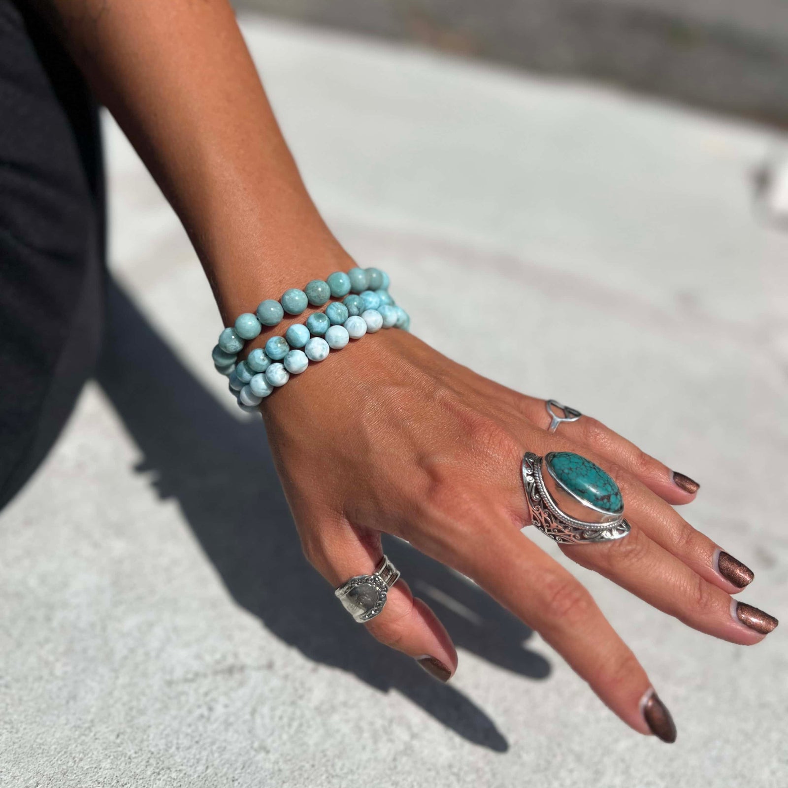 Hand wearing multiple Larimar bracelets and rings on a light background