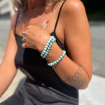 Woman wearing a black tank top and gray shorts with Larimar bracelets on her wrist.