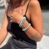 Woman wearing a black tank top and gray shorts with Larimar bracelets on her wrist.