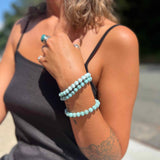 Woman wearing a black tank top and Larimar bracelets on a blurred outdoor background