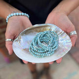 Person holding a shell with a Larimar beaded bracelet inside, wearing bracelets and rings.
