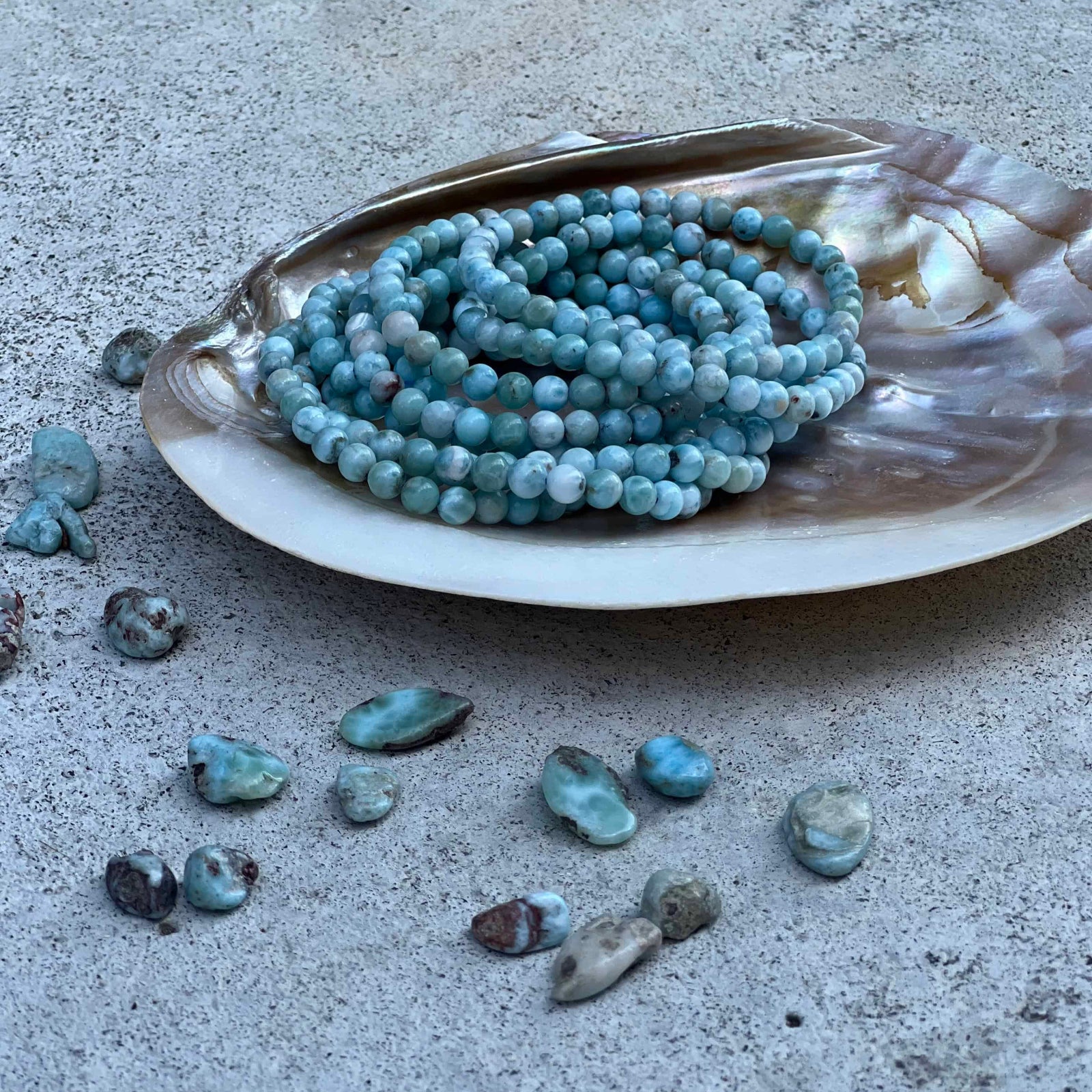 Larimar beads on a shell with scattered stones on a concrete surface