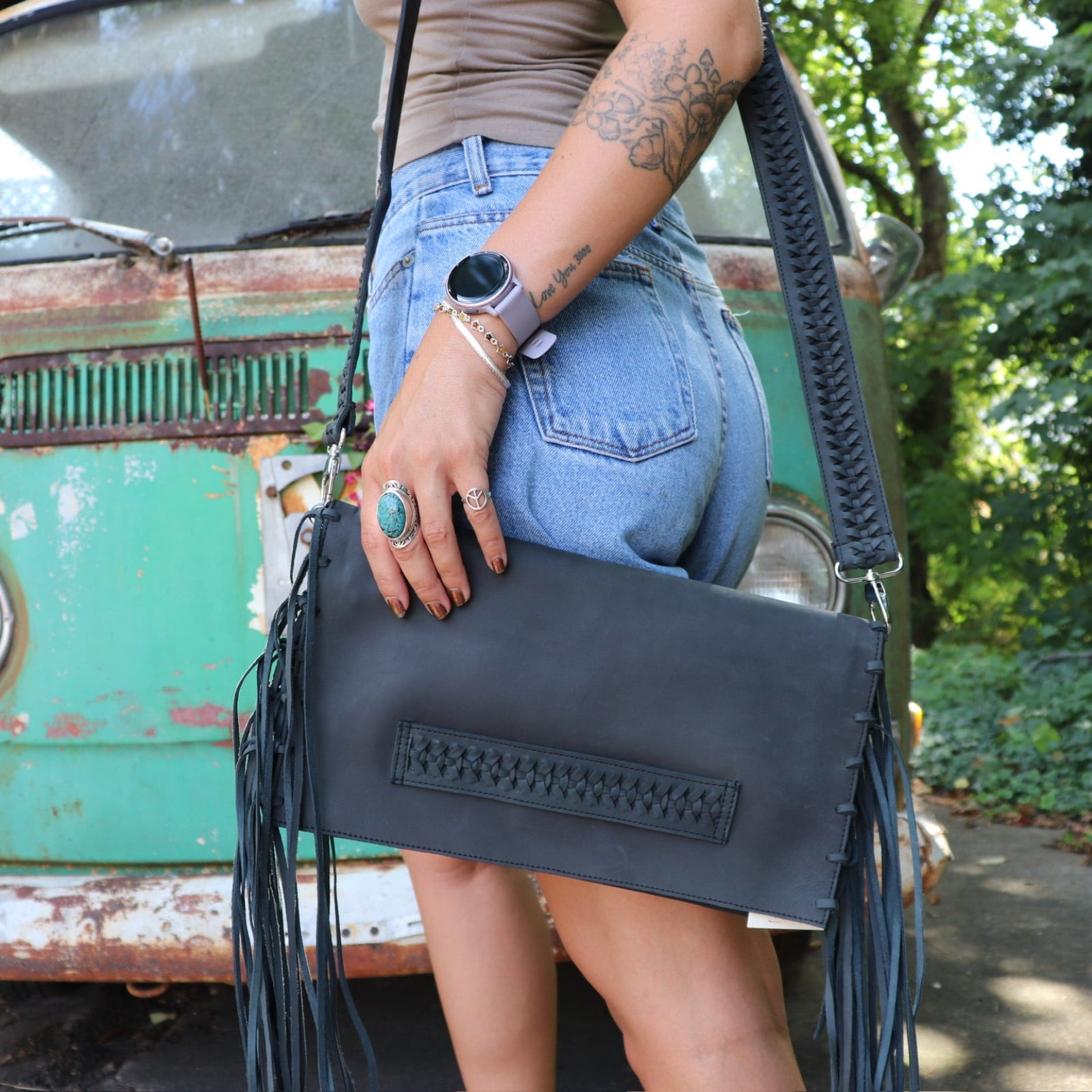Person holding a black leather clutch with fringe details in front of a vintage green van.