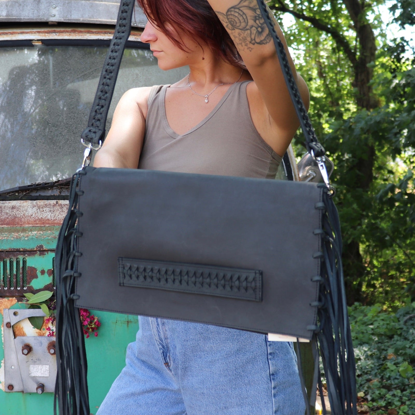 Person holding a black leather clutch handbag with fringe details outdoors.