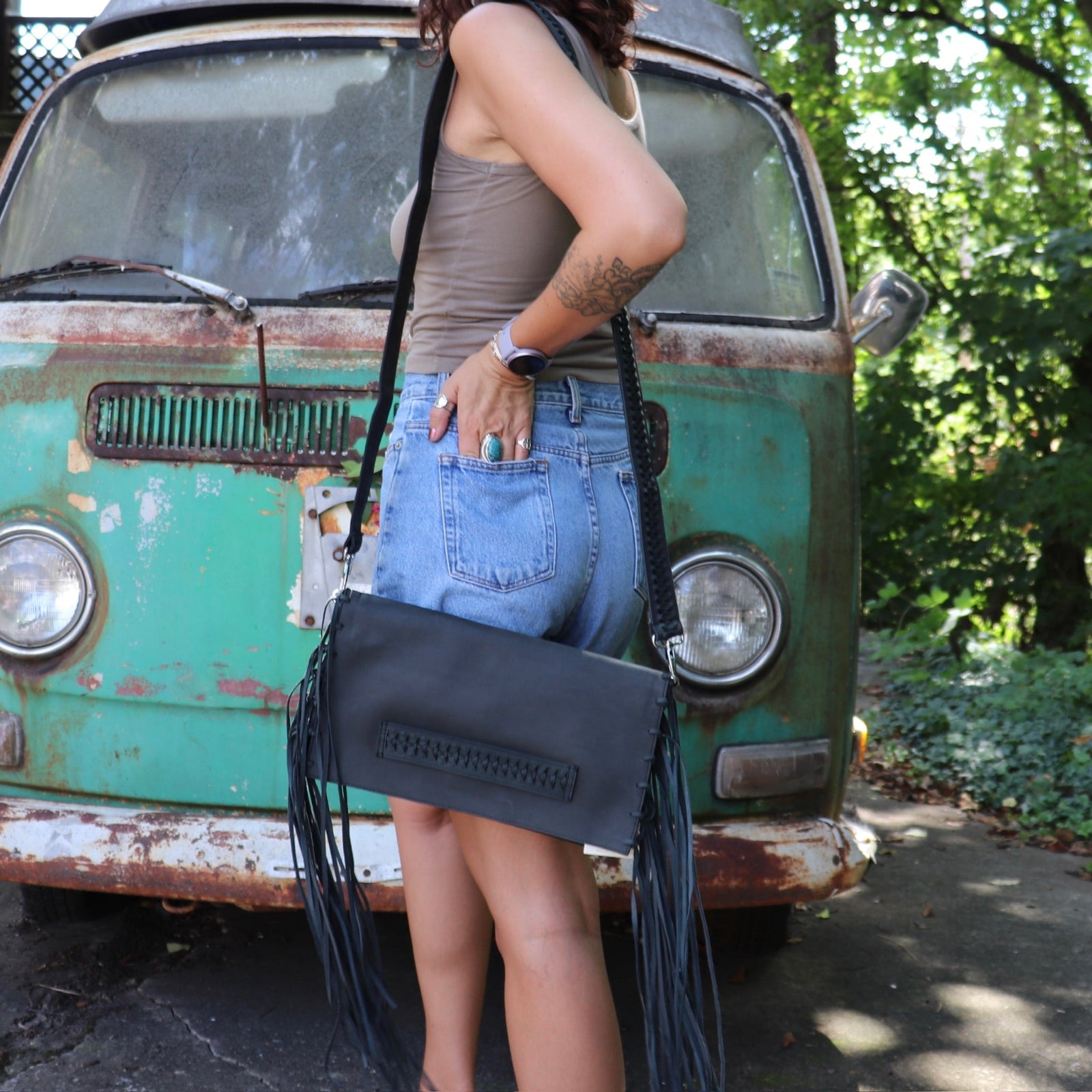 Person holding a black leather clutch handbag with fringe in front of a vintage green van.