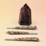 Holographic package of Manifest Magic Rollies with visible herbs inside, surrounded by individual rollies on a soft blush background