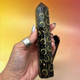 Hand holding a black crystal with gold moon and star patterns against a gradient background