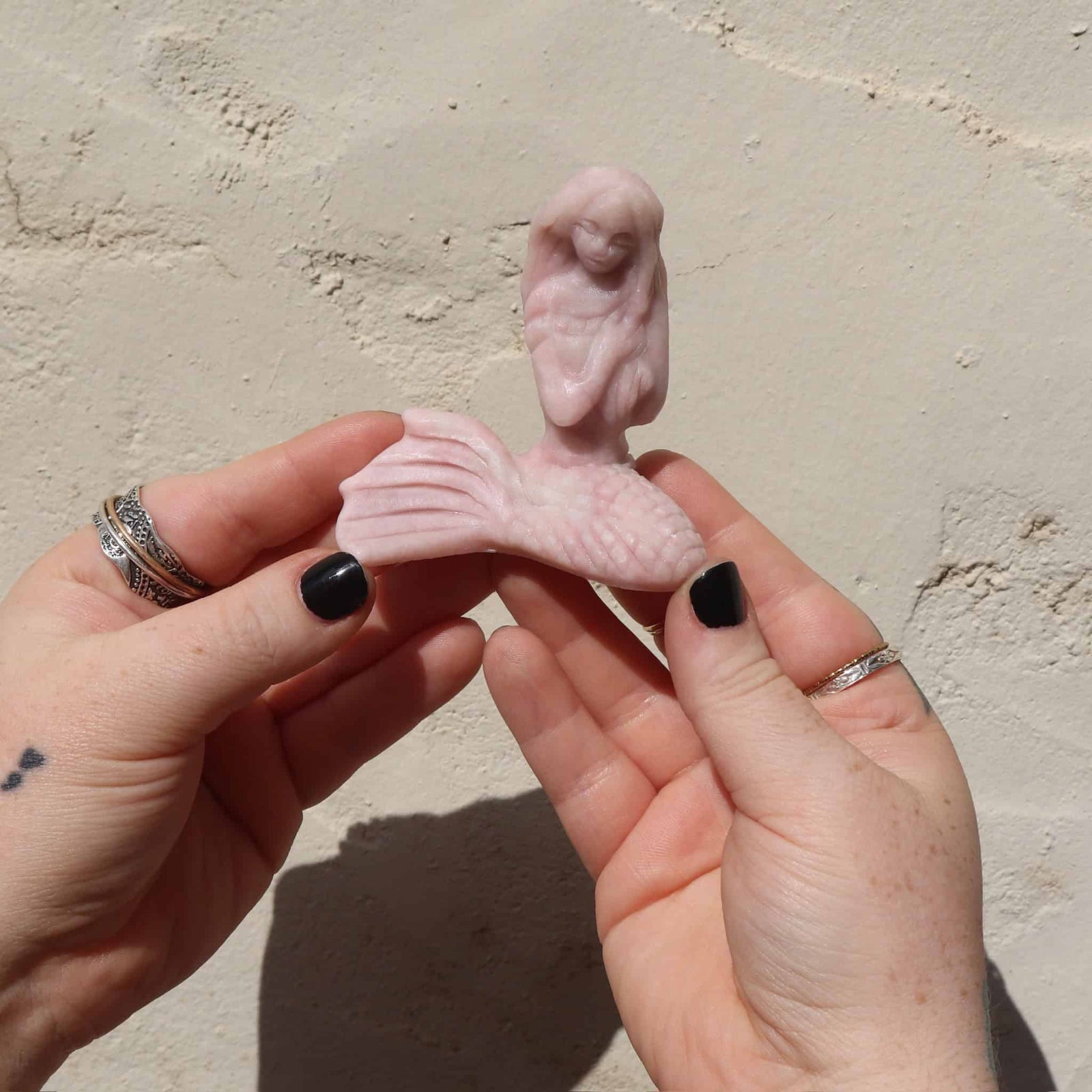 Pink opal crystal mermaid sculpture of a figure held between two hands against a beige background