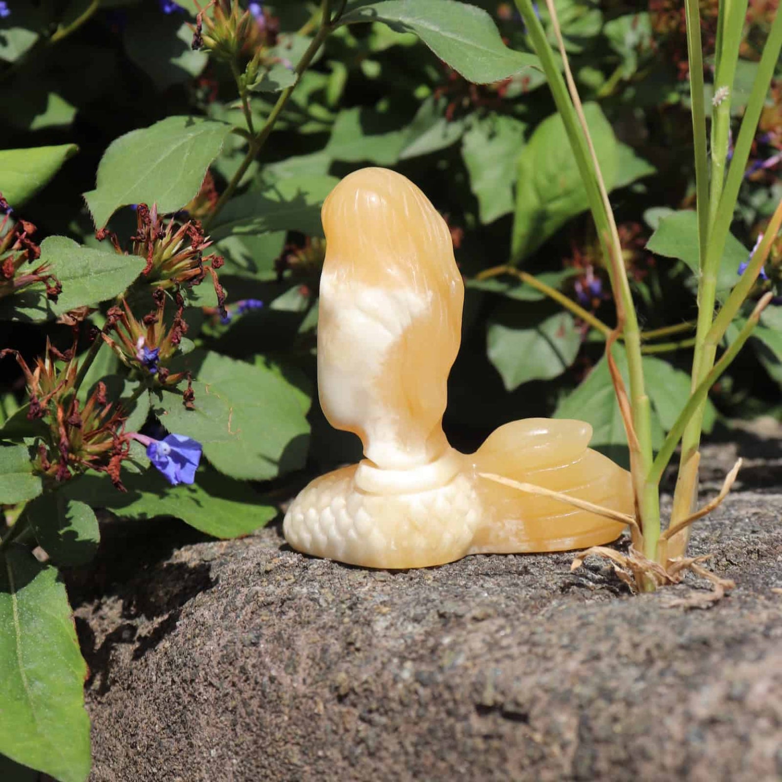 Decorative crystal orange calcite mermaid sculpture of a bird on a stone surface with greenery in the background