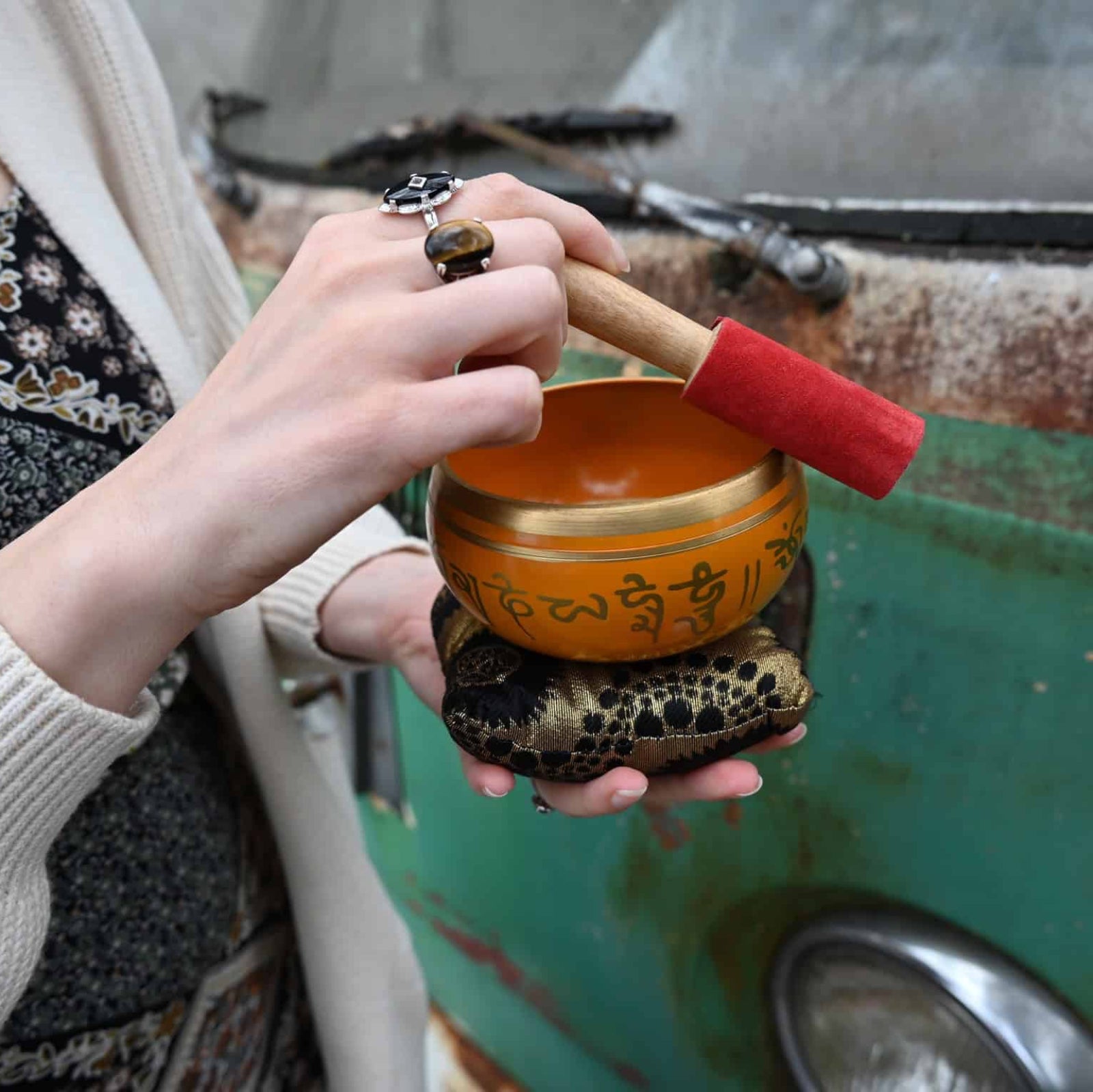 Person holding a small orange singing bowl with a red handle in front of a green metal surface.