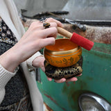 Person holding a small orange singing bowl with a red handle in front of a green metal surface.