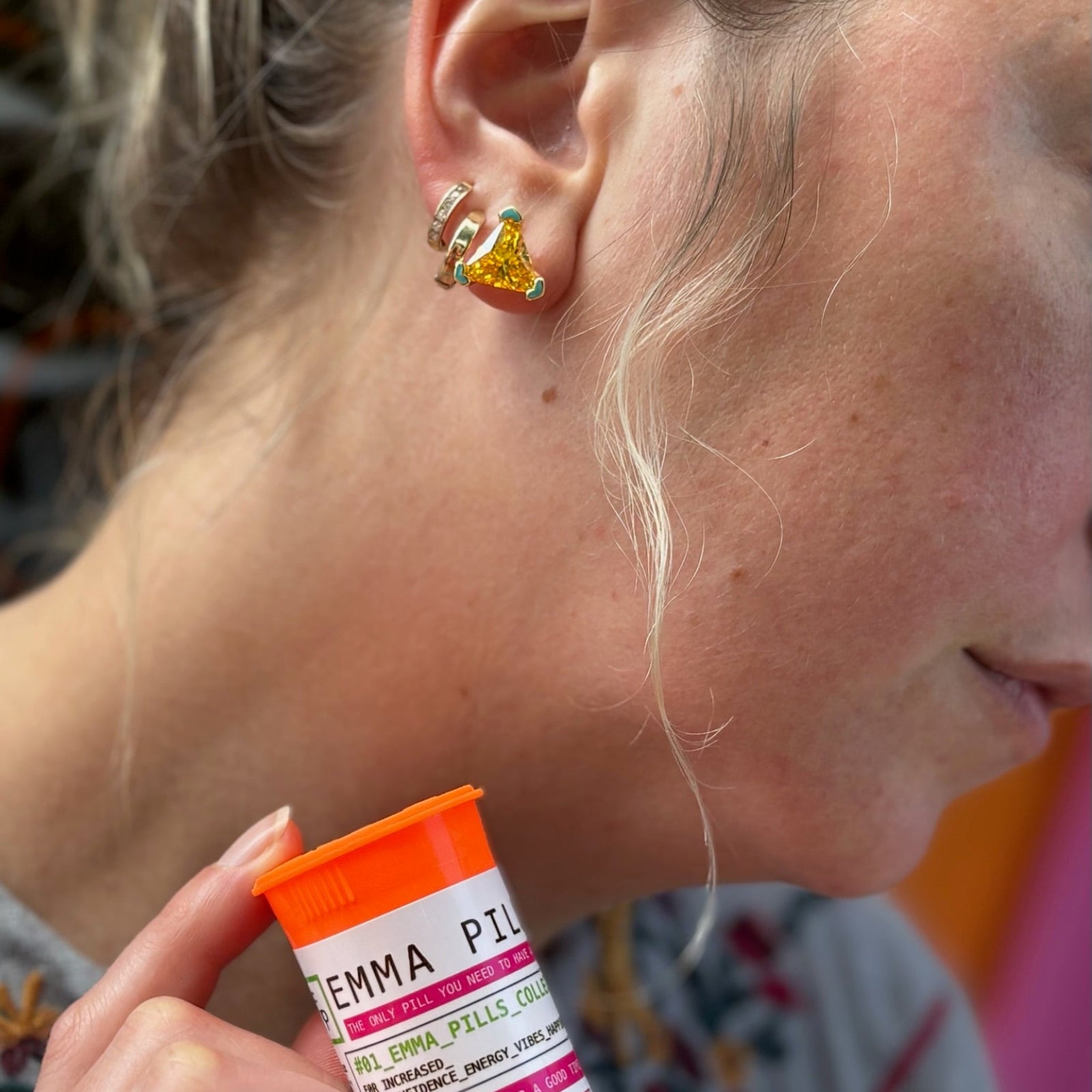 Own It Stud Earrings – Swarovski Crystal Studs close up shot of ear and model holding brand signature bottle