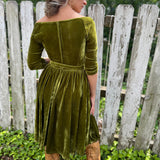 A woman wearing the 1950s Chartreuse Velvet Sweetheart Swing Dress in front of a wooden fence, showing off the back.