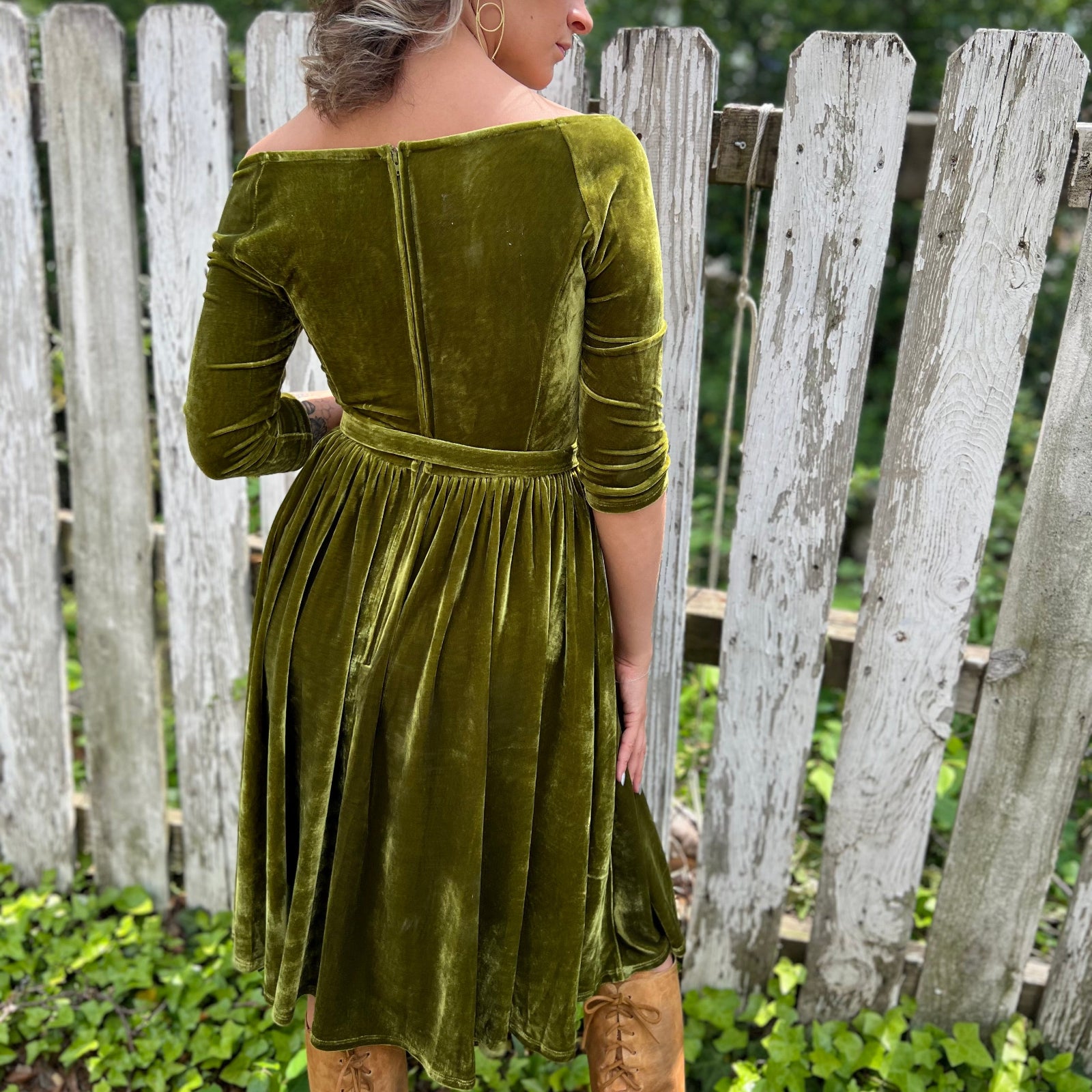 A woman wearing the 1950s Chartreuse Velvet Sweetheart Swing Dress in front of a wooden fence, showing off the back.