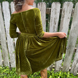 A woman wearing the 1950s Chartreuse Velvet Sweetheart Swing Dress in front of a wooden fence, showing off the back.