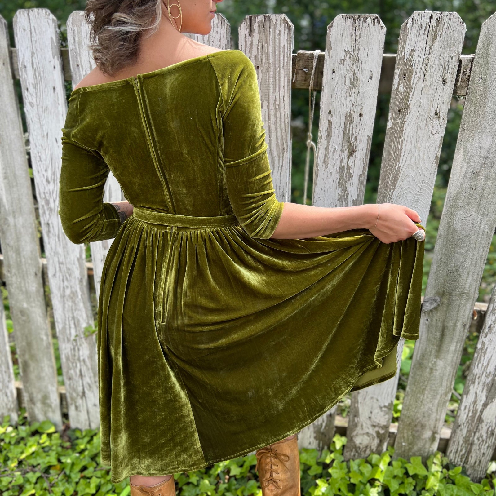 A woman wearing the 1950s Chartreuse Velvet Sweetheart Swing Dress in front of a wooden fence, showing off the back.