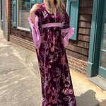 A woman wearing the 1960s Purple Floral Burnout Velvet Maxi Dress in front of a store front background.