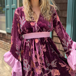 A woman wearing the 1960s Purple Floral Burnout Velvet Maxi Dress in front of a store front background, showing off the front details.
