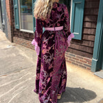 A woman wearing the 1960s Purple Floral Burnout Velvet Maxi Dress in front of a store front background, showing off the back.