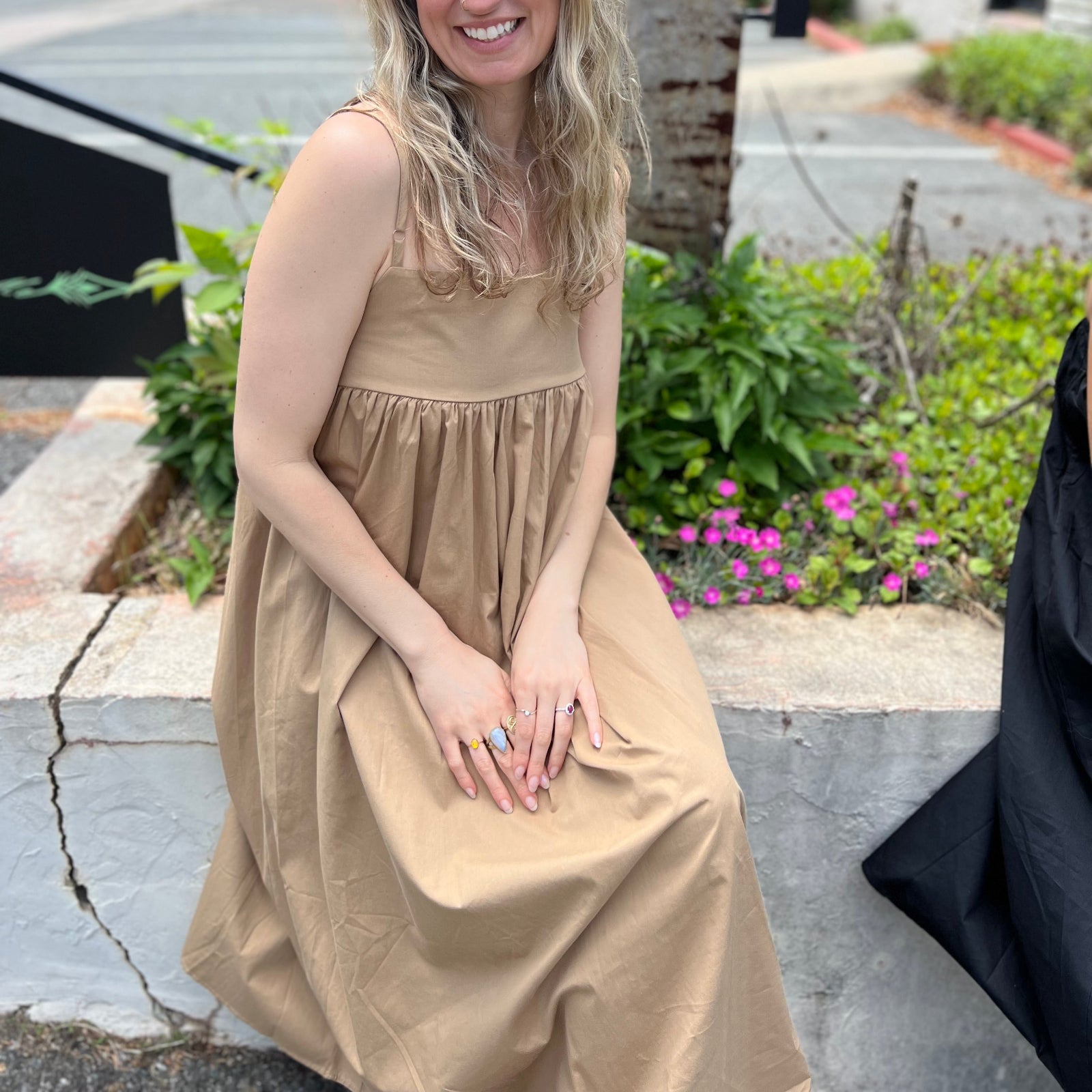 A woman wearing the khaki Solid Color Pleats Suspender Acetate Fiber Free Size Dress while sitting on a white ledge.